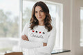 Woman wearing a white long-sleeve shirt with 'Canasta' design in a bright room.