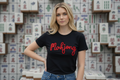 Woman wearing a black t-shirt with 'Mahjong' in red text, standing in front of a background of Mahjong tiles.