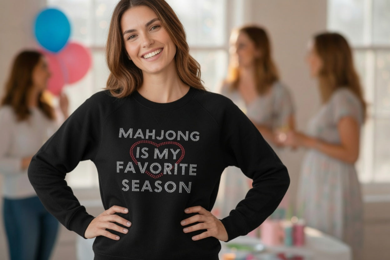 Woman wearing a black sweatshirt with 'Mahjong is my favorite season' text in a room with blurred people in the background.