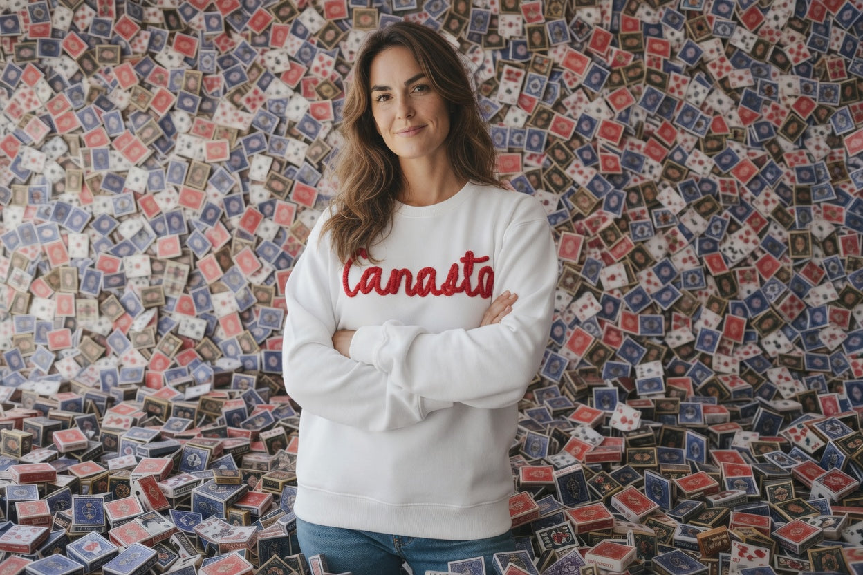Woman wearing a white sweatshirt with 'Canasto' text standing in front of a wall with a pattern of small colorful flags.