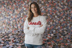 Woman wearing a white sweatshirt with 'Canasto' text standing in front of a wall with a pattern of small colorful flags.