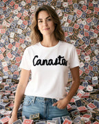 Woman wearing a white t-shirt with 'Canasta' text in front of a wall covered with playing cards.
