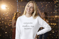 Woman wearing a white sweater with 'canasta makes me HAPPY!' text, standing in a cityscape at night.