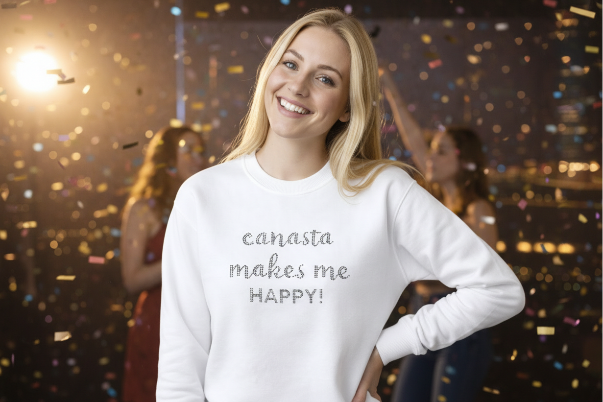 Woman wearing a white sweater with 'canasta makes me HAPPY!' text, standing in a cityscape at night.