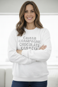 Woman wearing a white sweatshirt with 'CAVIAR CHAMPAGNE CHOCOLATE CANASTA' text.