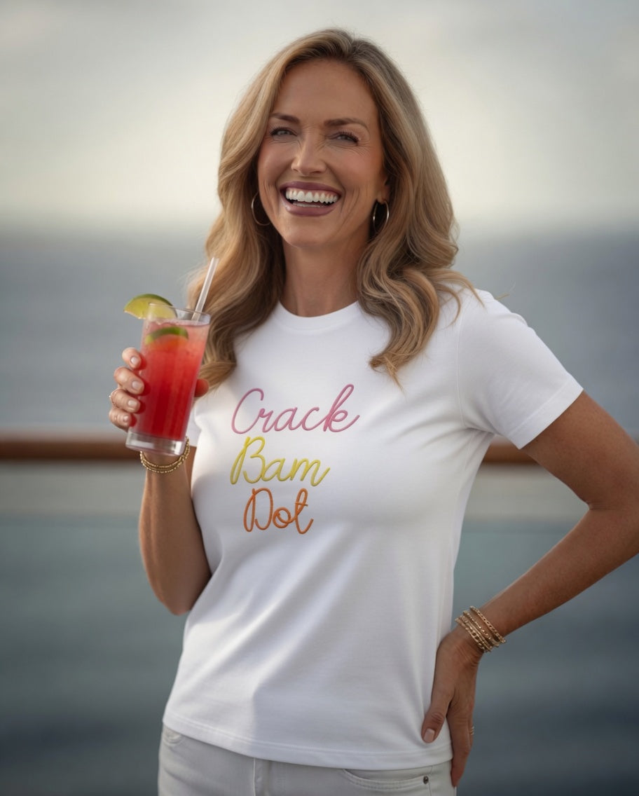 Woman wearing a white t-shirt with 'Crack Bam Dot' text, holding a drink by the water.