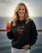 Woman wearing a black sweatshirt with colorful text, holding a drink by the water.