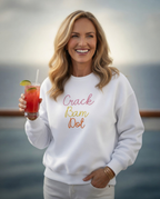 Woman wearing a white sweatshirt with 'Crack Bam Dot' text, holding a drink by the water.