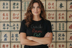 Woman wearing a white t-shirt with 'Crack Bam Dot' text in front of a wall with Chinese characters.
