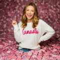 Woman wearing a white sweatshirt with 'Canasta' in pink, surrounded by playing cards against a patterned wall.
