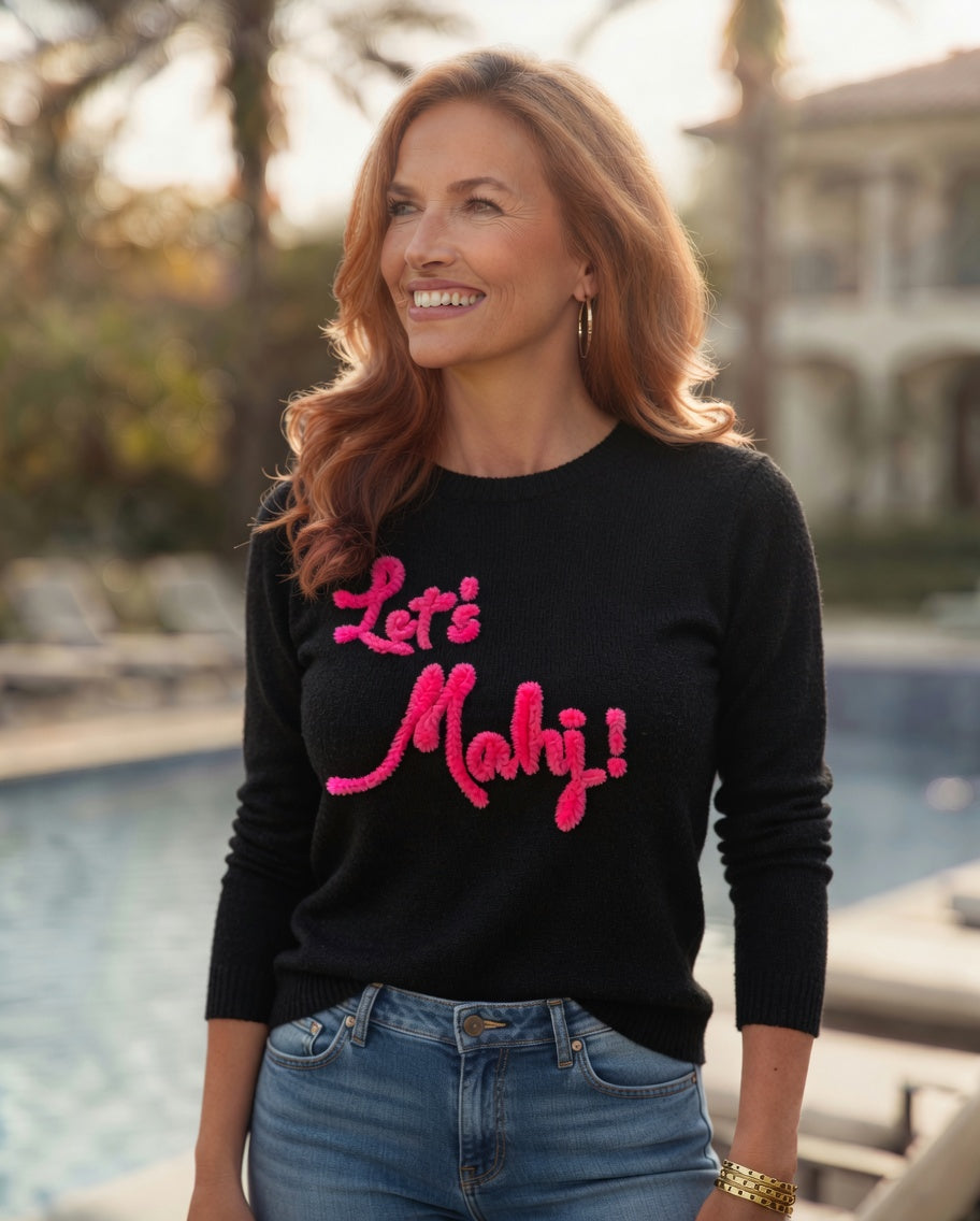 Woman wearing a black sweater with pink Let's Mahj text, standing by a pool.