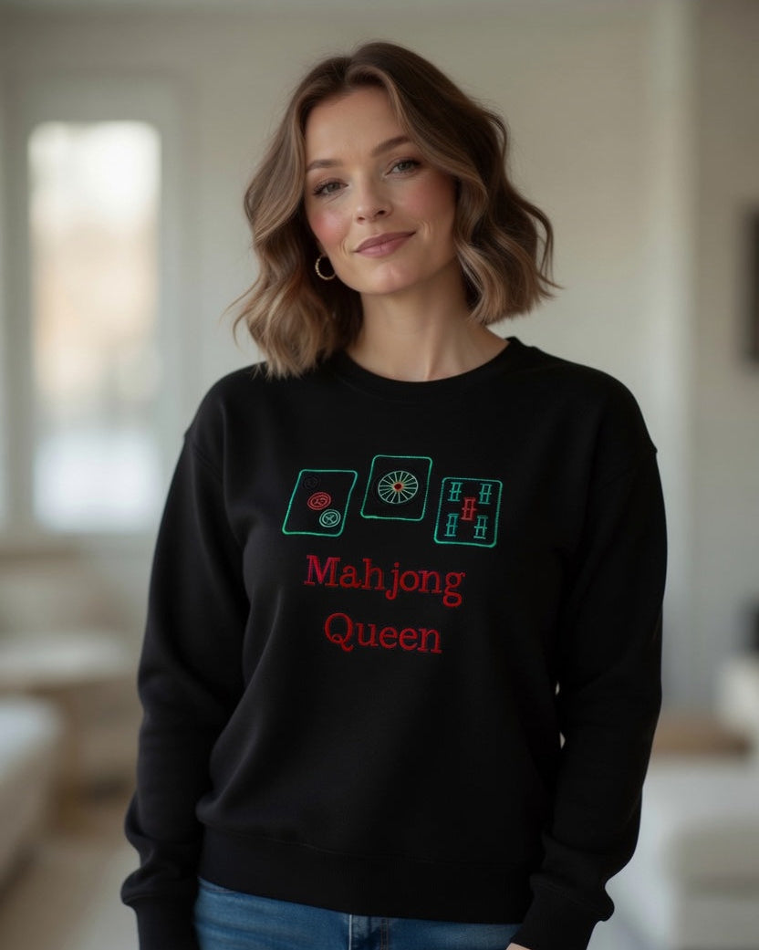 Woman wearing black sweatshirt pullover tee with embroided mahjong queen design in interior settings